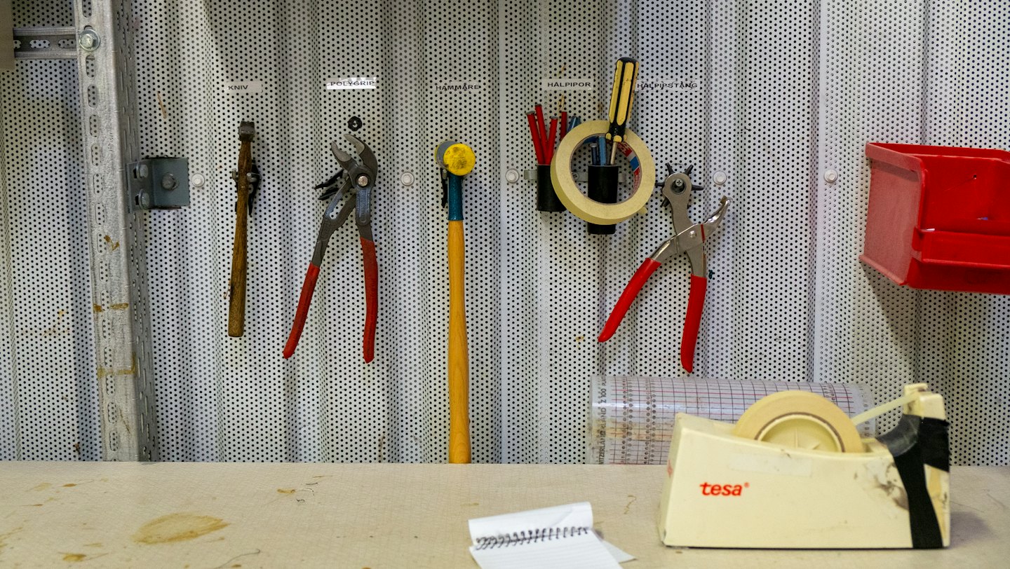 Attrezzi da lavoro ordinatamente disposti su un pannello forato sopra un banco da lavoro artigianale.